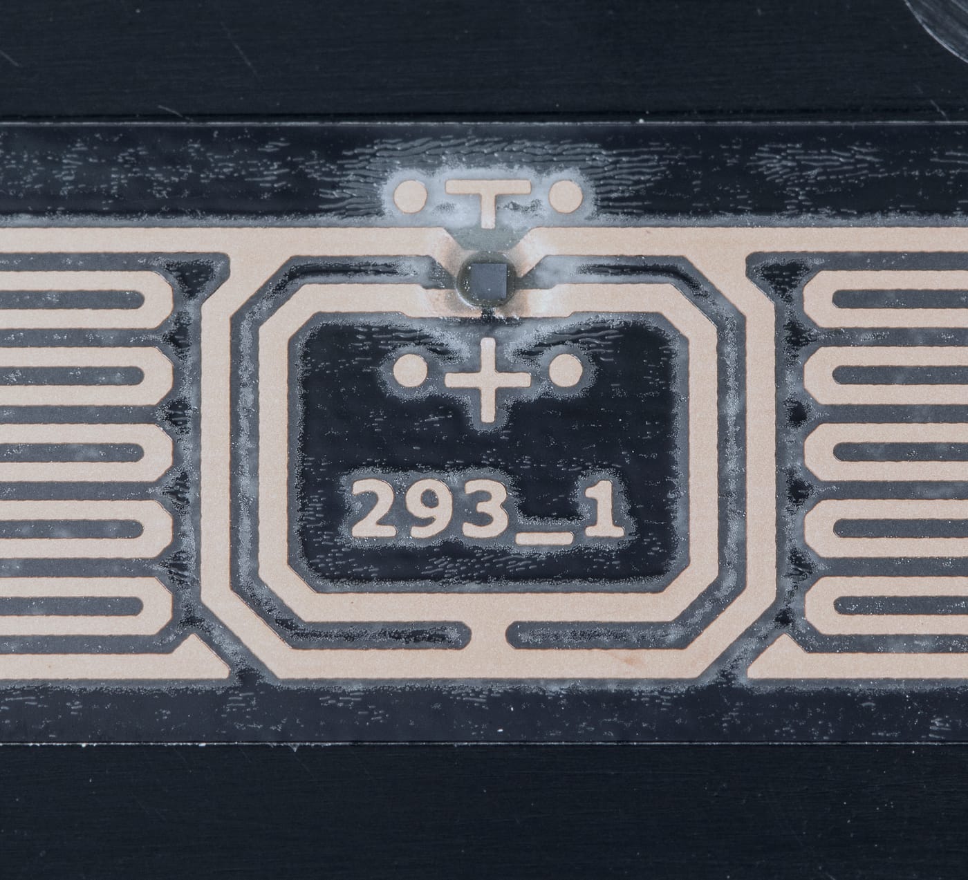 A macro photograph of a UHF RFID inlay: a copper dipole antenna with comb-shaped end loops and a small silicon chip, on clear adhesive film over black plastic.
